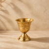 Verre artisanal en cuivre doré posé sur un fond beige, avec motifs gravés et finition brillante.
